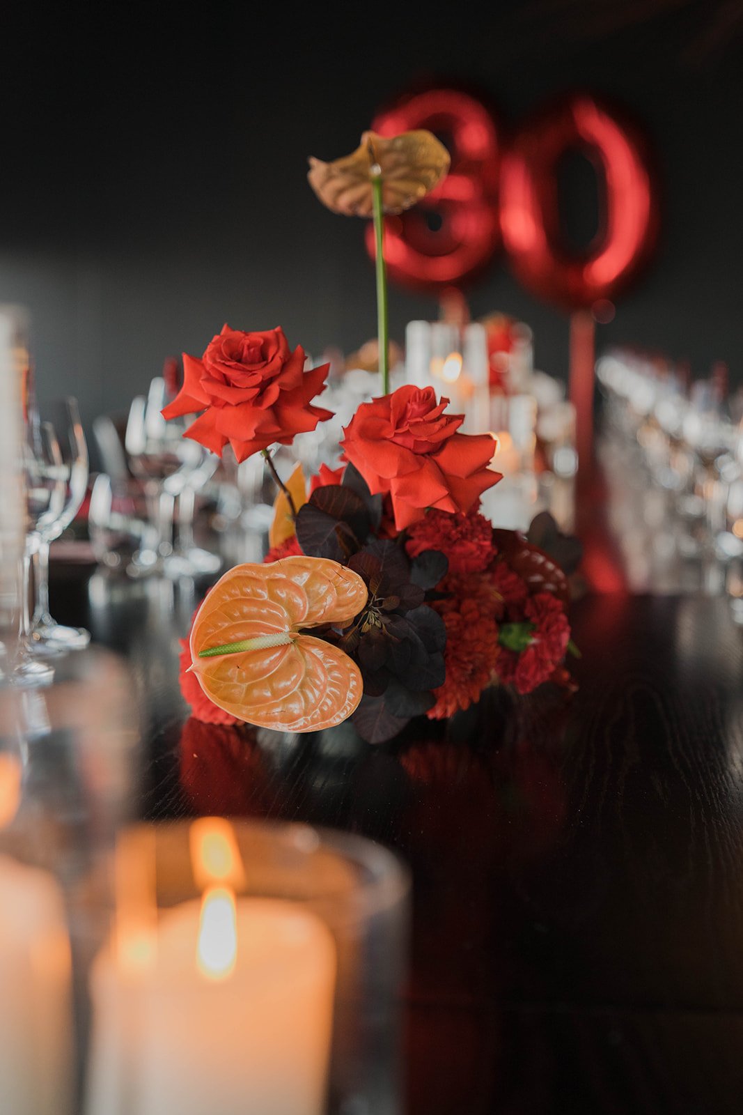 A vibrant floral setting with bright orange and deep reds sit behind a burning candle. A bright-popping red 30 balloon sits behind the florals for a 30th Birthday celebration in Melbourne. 