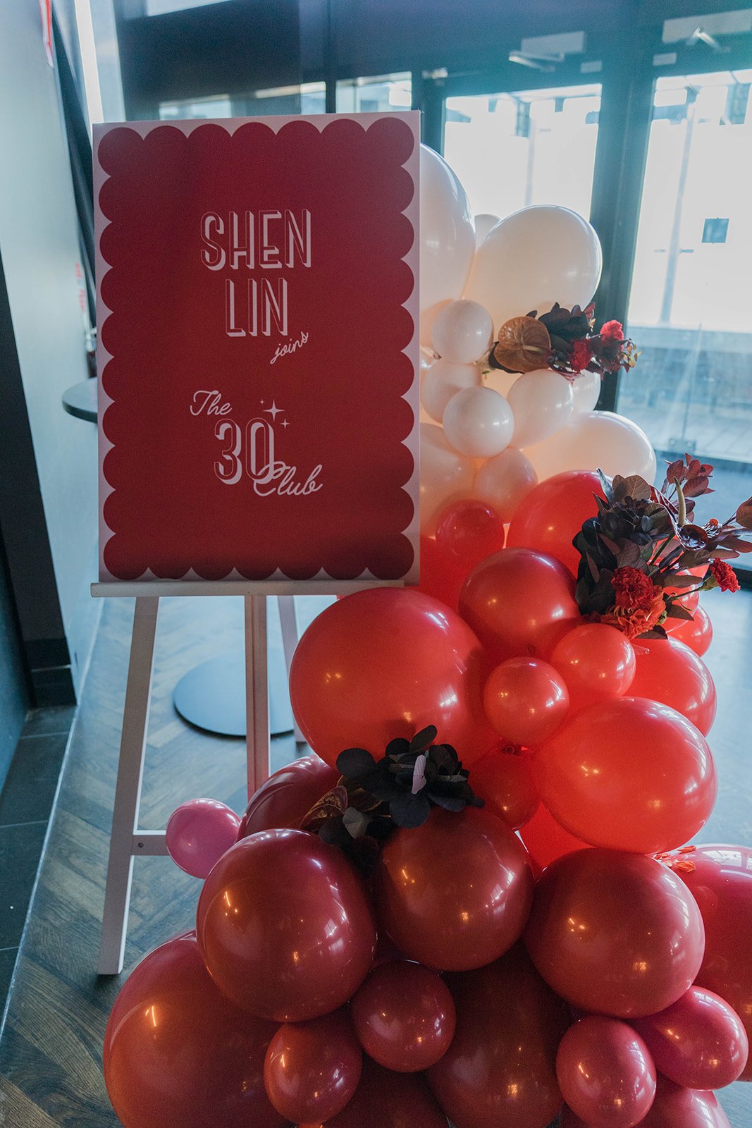 Birthday party welcome sign with balloon garland flowing down from the sign, filled with floral bouquets in deep reds. Hosted in a high-end Melbourne restaurant. 