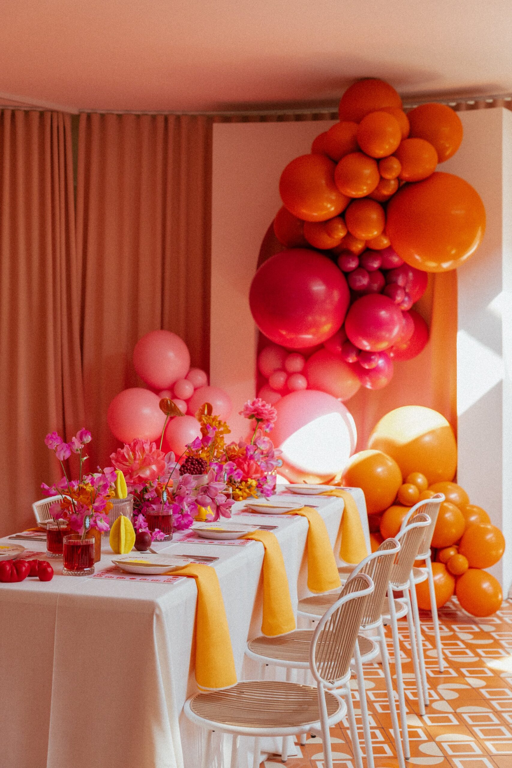 A pretty and pink bridal shower table setting, with a hot pink and vibrant orange balloon garland cascading down an arch, at a event space in Melbourne.