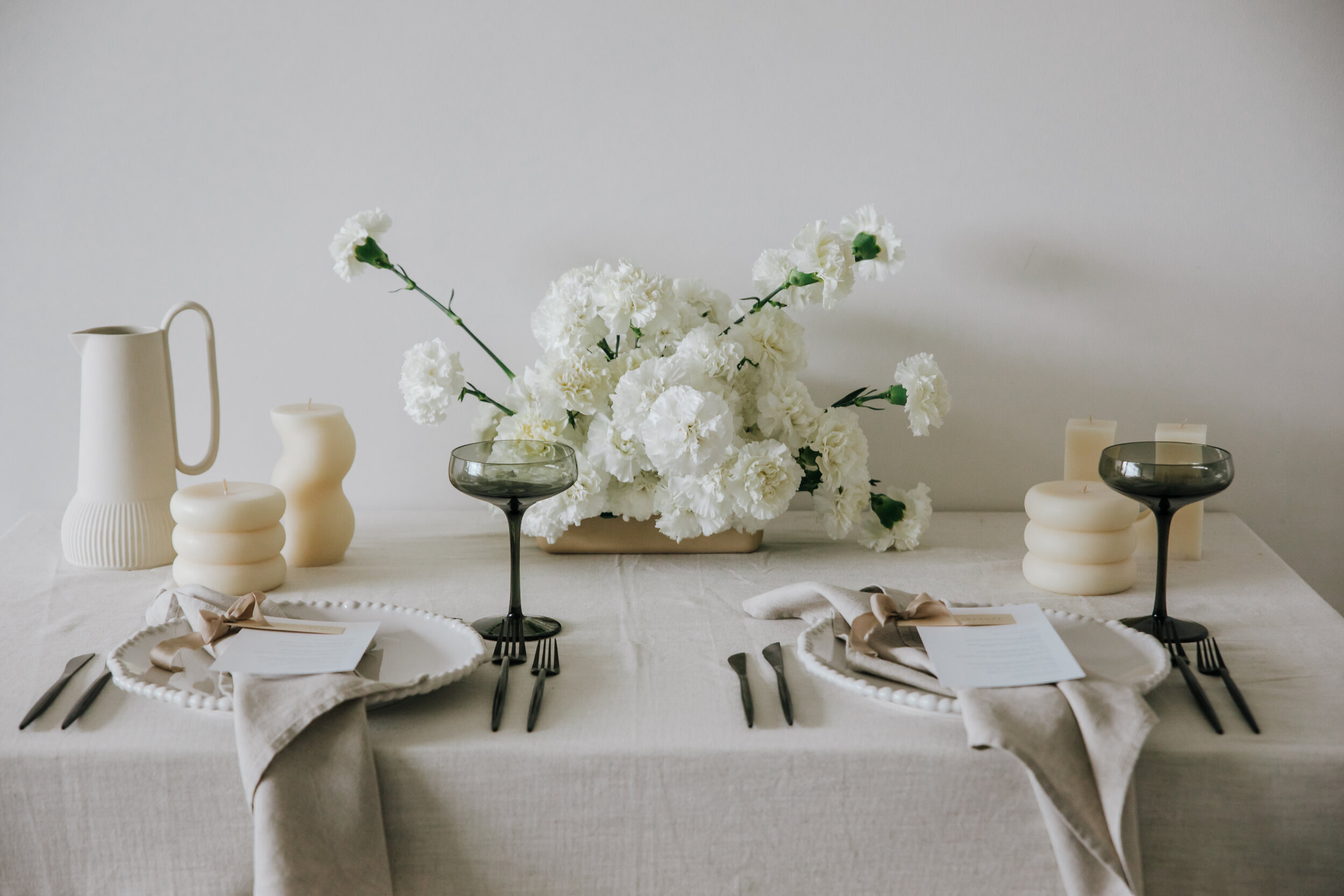All images were captured by the wonderful Susie from Light Gloss, who is known for her premium and perfectly moody editing. A table setting with white florals, lined table cloth and dark cutlery and glasses. 