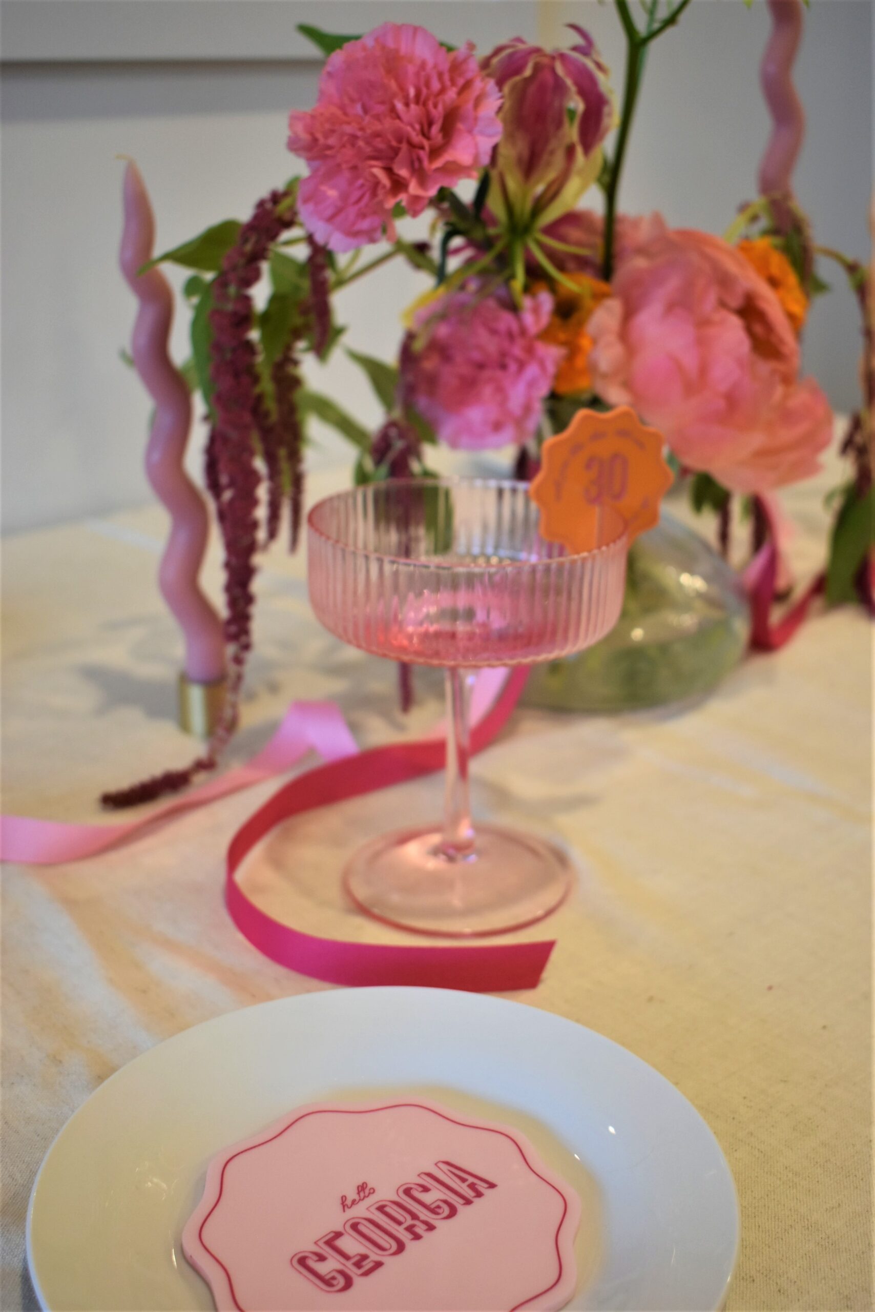 A personalised pink wavey drinks coaster in a table setting with martini glass, drinks tag and florals in the background. Styled and delivered by Coral & Co. 